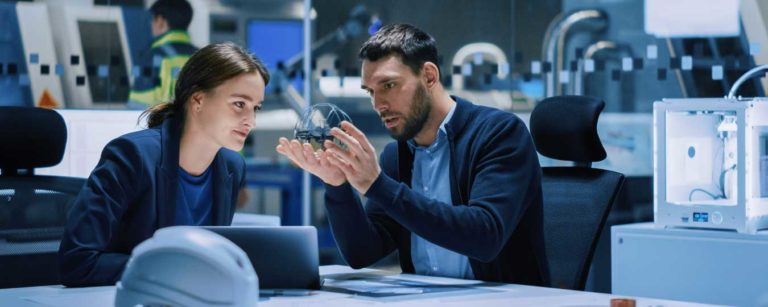 Woman and man looking at product during R&D in office with hard hat on table
