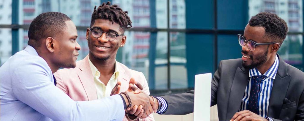 Image of three men at table with laptop and two shaking hands